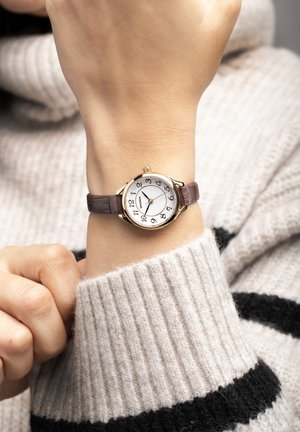 Montre dorée avec un cadran blanc, des chiffres noirs et un bracelet en cuir marron. Présente un boîtier rond et un mécanisme de remontage couronné.