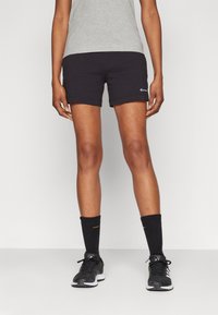 Shorts deportivos negros con una textura suave, con un logo en el dobladillo, combinados con calcetines negros y zapatillas de correr.