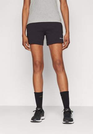 Shorts deportivos negros con una textura suave, con un logo en el dobladillo, combinados con calcetines negros y zapatillas de correr.