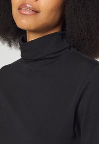 Schwarzer Baumwoll-Rollkragenpullover mit glatter Textur, hohem Kragen und figurbetontem Design. Mit minimalen Nähten für ein sauberes Aussehen verziert.