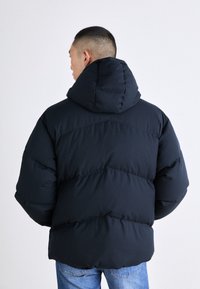 Marinblå vadderad jacka med huva, med quiltad design och tjock vaddering. Jackan har en avslappnad passform och mjuk textur.