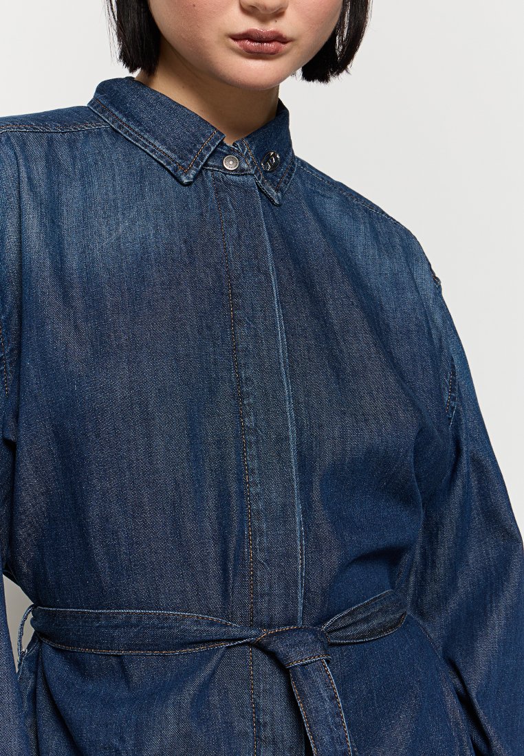 Robe chemise en denim bleu foncé avec un col structuré, des boutons sur le devant, une ceinture à la taille et des manches longues. Présente des détails de couture subtils.