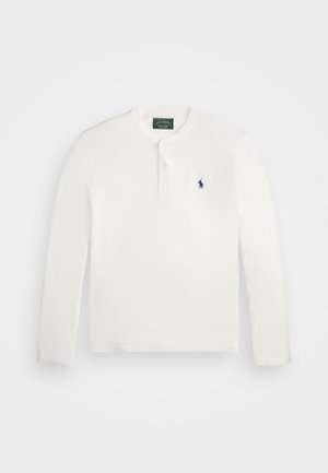 Långärmad vit bomullsskjorta med henley-krage, tre knappar och en liten blå broderad logotyp på bröstet.