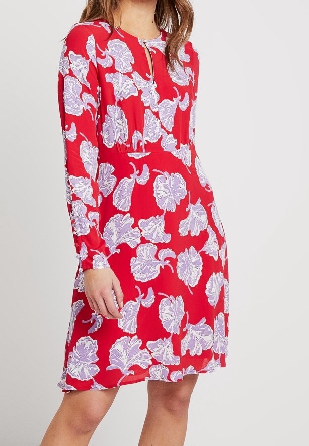 Femme portant une robe rouge mi-longue avec des manches longues et de grands motifs floraux blancs et violet clair.