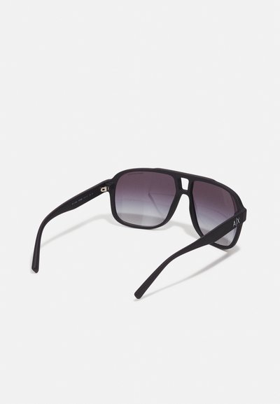 Lunettes de soleil noires avec un design de monture plate, verres dégradés et texture mate. Présente un logo argenté sur la branche.