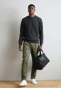 Pull noir, pantalon vert olive et baskets blanches. Tient un sac de sport noir à double sangle. Design simple et décontracté.