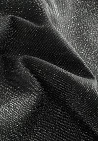 Černá látka se třpytivou stříbrnou texturou, se soft a hladkým povrchem a mírně zmačkaným vzhledem, vykazující hru světla.