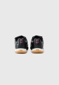 Par svart joggesko med hvite mellomsåler og slett brune yttersåler, sett bakfra, med en rosa rund logo på hver hæl.