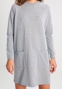 Grå sweatshirtklänning i mjukt material, med långa ärmar, rund halsringning och två framfickor. Enkelt och avslappnat design.