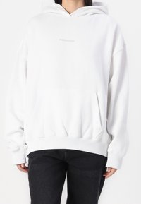 Sweat à capuche blanc surdimensionné avec une poche avant, des poignets et un ourlet côtelés, arborant un logo texte gris subtil "PEGADOR" sur la poitrine.