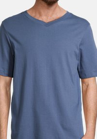 V-ringad T-shirt i ett mjukt, enfärgat blått tyg. Korta ärmar, avslappnad passform, med en slät yta och minimal sömdetalj.