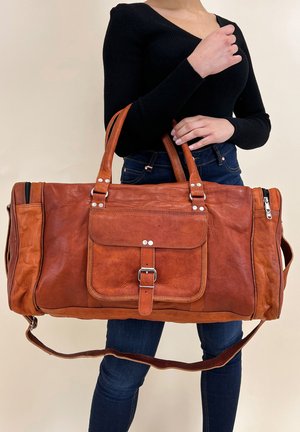 Brūns ādas duffel soma ar priekšējo kabatu, sudraba aparatūru un diviem rokturiem. Aprīkota ar noņemamu plecu siksnu un teksturētu virsmu.