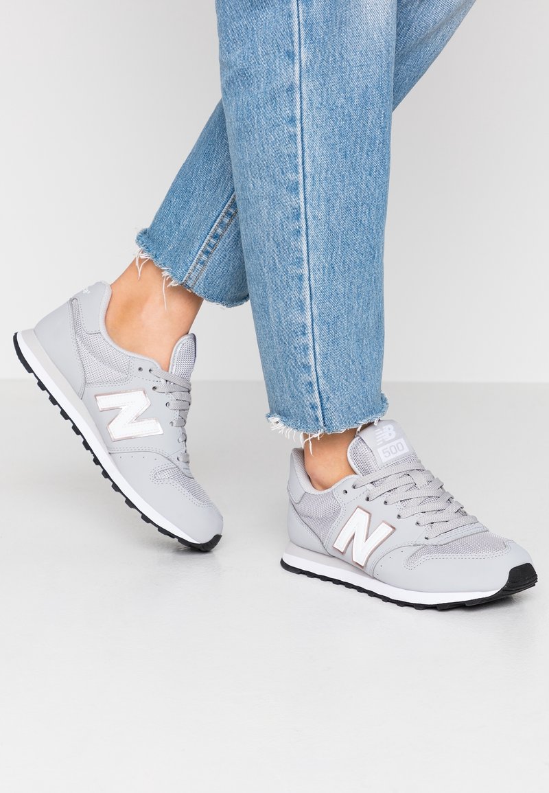 Graue New Balance 500 Sneaker mit Obermaterial aus Mesh und Synthetik, weißen Akzenten, Gummisohle und gepolstertem Kragen, kombiniert mit ausgefransten Denim-Jeans.