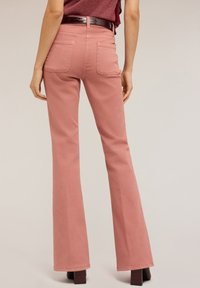 Jeans de campana rosa hechos de una mezcla de algodón, con dos bolsillos traseros y una cintura alta. Combinados con un cinturón burdeos brillante.