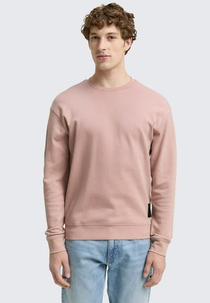 Rosa Baumwoll-Sweatshirt mit langen Ärmeln, gerippten Bündchen und Rundhalsausschnitt, kombiniert mit hellblauen Jeans. Schwarzes Etikett am Saum.
