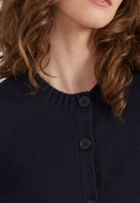 Cardigan navy con colletto a costine, caratterizzato da quattro bottoni neri sulla parte frontale e una trama fine. Cuciture visibili aggiungono dettagli.