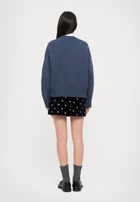 Paks sinine kootud sviiter ümmarguse kaelusega, ribakujuliste varrukate ja võimalusega; on kombineeritud musta seeliku ja hõbedaste kaunistustega.