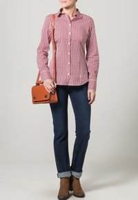 Punainen ja valkoinen ruudullinen napitettava paita, farkut, ruskeat nilkkasaappaat ja pieni ruskea laukku, jossa on läppä ja kaksi hopeista solkea.