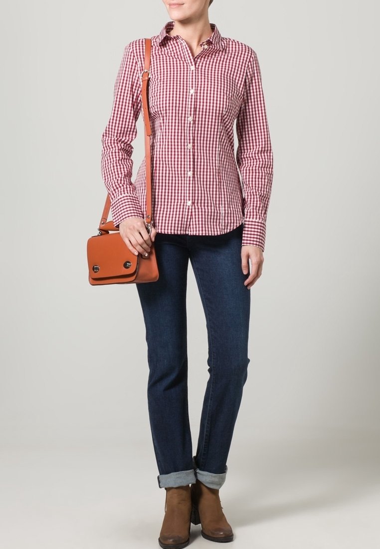 Punainen ja valkoinen ruudullinen napitettava paita, farkut, ruskeat nilkkasaappaat ja pieni ruskea laukku, jossa on läppä ja kaksi hopeista solkea.