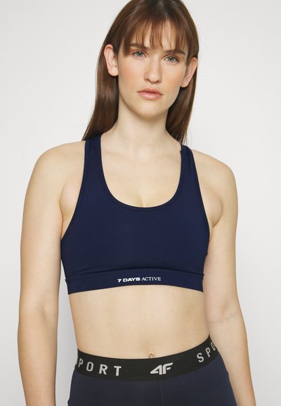 Navy blue sports bra with a rounded neckline and wide straps. Features a logo band with "7 DAYS ACTIVE" in white. Smooth texture.
