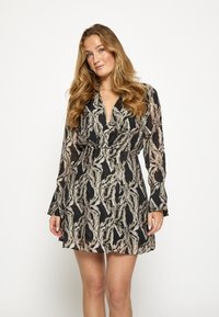 Vestido negro de manga larga con un patrón abstracto en espiral en beige y gris, con escote en V profundo y cintura ajustada, que se extiende hacia un dobladillo acampanado.