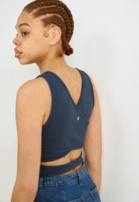 Navy blue sports bra with a textured fabric, crisscross back design, and a small logo detail. Paired with high-waisted denim shorts.