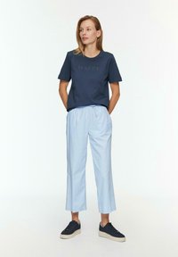 Marineblaues Baumwoll-T-Shirt mit "HAPPY" in hellerer Schrift aufgestickt, kombiniert mit hellblauen, locker sitzenden, cropped Pants und dunklen Sneakers.