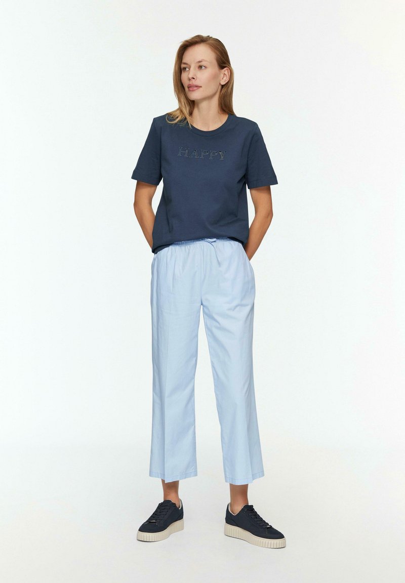 Marineblaues Baumwoll-T-Shirt mit "HAPPY" in hellerer Schrift aufgestickt, kombiniert mit hellblauen, locker sitzenden, cropped Pants und dunklen Sneakers.