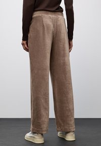 Bruine corduroy wijde broek met een zachte textuur, voorzien van een ontspannen pasvorm en zichtbare stikseldetails, gecombineerd met lichtgekleurde sneakers.