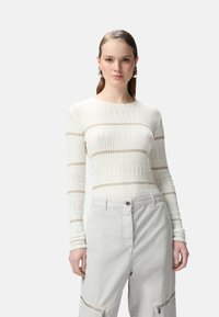 Maglietta leggera a maniche lunghe a righe ribattute in bianco con sottili strisce beige. Abbinata a pantaloni grigi chiari con zip e chiusura a bottone.