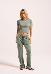 Zelené cropované tričko s nápisem "bust", doplněné o volné zelené sametové kalhoty s elastickým pasem a bočními kapsami.