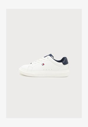 Λευκό low-top αθλητικό παπούτσι με σκούρο μπλε γιακά φτέρνας, κορδόνια και μικρό κόκκινο, λευκό και μπλε λογότυπο στο πλάι, σε απλό φωτεινό φόντο.