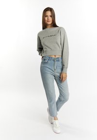 Grijze cropped sweatshirt met geborduurde tekst, gecombineerd met lichtblauwe jeans en witte sneakers; zachte stof, relaxed pasvorm en casual stijl.