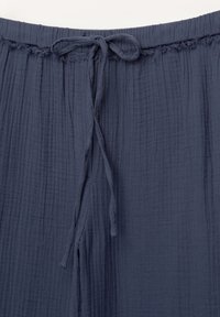 Dunkelblaue, strukturierte Stoffhosen mit einem elastischen Bund und einer gebundenen Kordel. Verfügt über weiche, gerüschte Details entlang der oberen Kante.