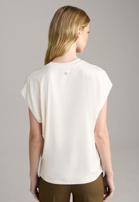 Weißes Kurzarmoberteil mit Rundhalsausschnitt und kleinem Logo-Detail am Rücken, gefertigt aus glattem, leichtem Stoff und in entspannter Passform.