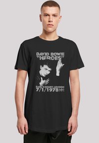 Black t-shirt featuring a graphic of David Bowie, with text: "HEROES!" and concert details, in white and gray font. Short sleeves, crew neck.