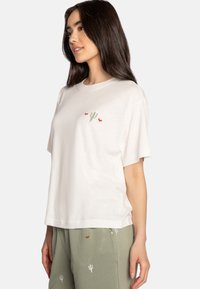 T-shirt bianca in cotone con ricamo di un cactus verde e un cuore rosso sul petto, maniche corte e vestibilità rilassata.