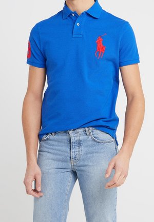 Blauwe polo in katoen met korte mouwen, voorzien van een rood geborduurd logo op de linkerborst en een klassiek kraagontwerp.