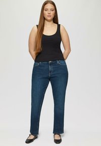 Débardeur sans manches noir associé à un jean droit bleu foncé, avec des poches avant et une fermeture éclair. Texture de denim lisse.