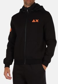 Felpa con zip nera dal design aderente, con un logo arancione sul petto e un accento sul braccio. Realizzata in tessuto morbido.