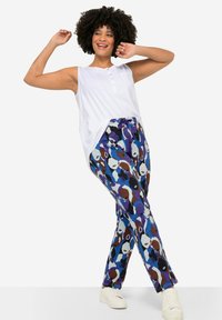 Witte mouwloze top met een knoopsluiting, gecombineerd met kleurrijke gestreepte broek met abstracte gezichten in blauwe, bruine en paarse tinten.