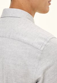 Camicia grigia con colletto e tessuto strutturato. Il collo presenta un design pulito e semplice, con cuciture visibili sul retro.