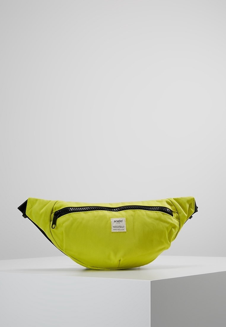 Sac banane de marque Anello vert vif avec fermeture éclair noire et sangles réglables, posé sur un piédestal blanc sur un fond uni.