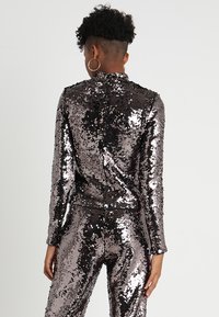 Glänzendes, dunkelsilbernes Pailletten-Zweiteiler-Outfit mit langen Ärmeln, tailliertem Schnitt und hohem Kragen, von hinten betrachtet. Keine sichtbaren Muster.