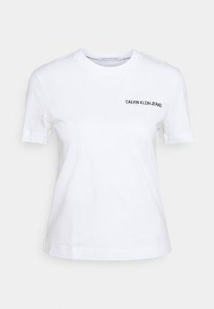 Biały t-shirt z krótkim rękawem i okrągłym dekoltem, z napisem „CALVIN KLEIN JEANS” nadrukowanym na lewej piersi.