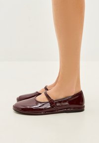 Burgunderfarbene Lacklederschuhe mit runder Zehenpartie, ausgestattet mit einem dekorativen Riemen und Schnallen-Details. Flache Sohle, schlichtes und klassisches Design.