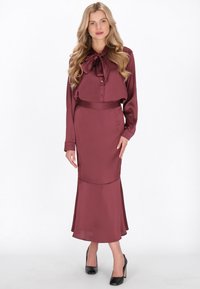 Vínová saténová halenka s mašlí na krku a odpovídající tužková sukně s rozšířeným lemem, doplněné černými vysokými botami na podpatku.