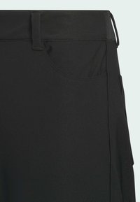 Primer plano de pantalones negros que muestra el bolsillo frontal, la trabilla del cinturón y detalles de las costuras sobre un fondo claro.