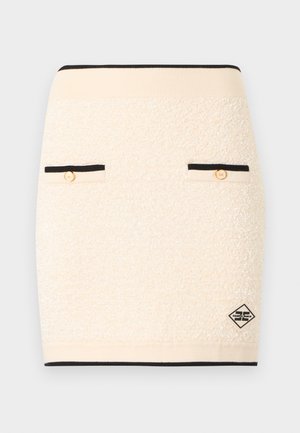 Minigonna in tessuto crema con bordi neri, due tasche frontali con bottoni dorati e una piccola patch con il logo del marchio in bianco e nero.