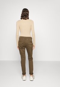 Khaki byxor med en smal passform, med en texturerad yta, uppvridna fållar och bakfickor med subtil detaljer. Kombinerat med vita sneakers.